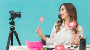 Explosão do Marketing de Influenciadores: Tendências para 2025 com criadora de conteúdo sorrindo enquanto grava vídeo para redes sociais segurando ícones de curtidas em um estúdio colorido.